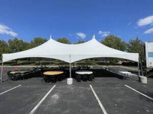 A white tent with tables and chairs in a parking lot.